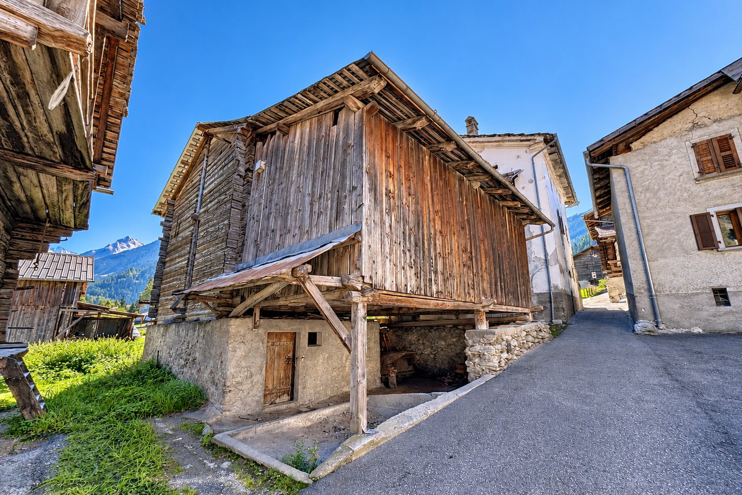 Le raccard côté ruelle : soubassement de pierre avec sa porte de bois, étages en bois patiné, voisinage de ruraux.