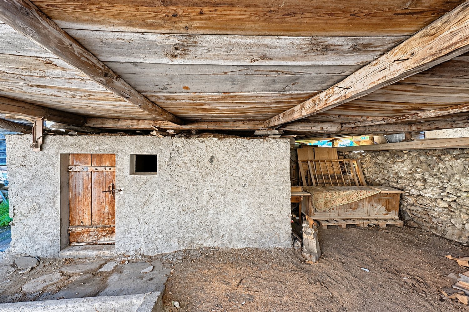 Sous le raccard : le soubassement maçonné, ses solives de bois, une porte et un mur de pierre sèche.